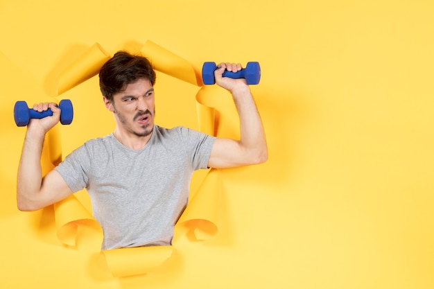 Jeune homme travaillant avec des haltères bleus sur fond jaune athlète sport gym