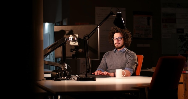 Jeune homme travaillant sur ordinateur la nuit dans un bureau sombre. Le dessinateur travaille plus tard.