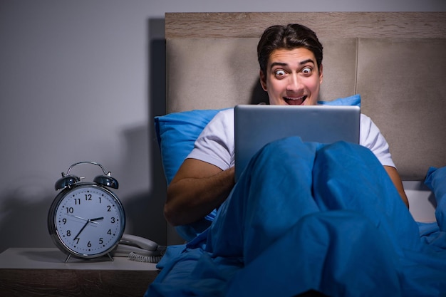 Jeune homme travaillant sur un ordinateur portable au lit