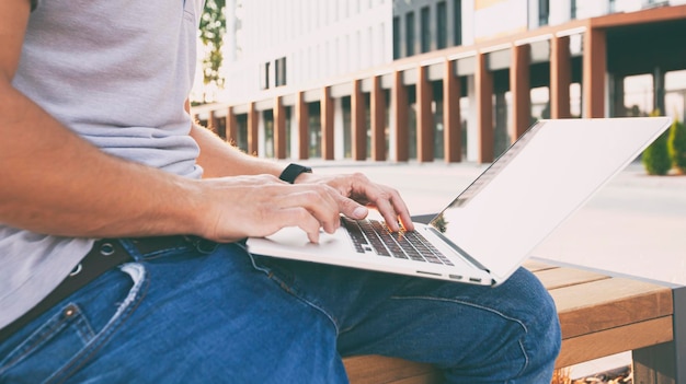 Jeune homme travaillant sur ordinateur portable un moment assis sur le banc