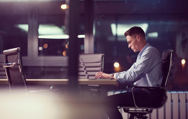 Jeune homme travaillant sur ordinateur portable la nuit dans un bureau sombre. Le dessinateur travaille plus tard.