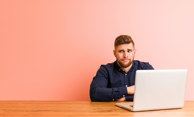 Jeune homme travaillant avec son ordinateur portable confus, se sent douteux et incertain