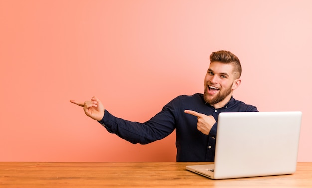 Jeune homme travaillant avec son ordinateur portable excité tenant un espace de copie sur la paume.