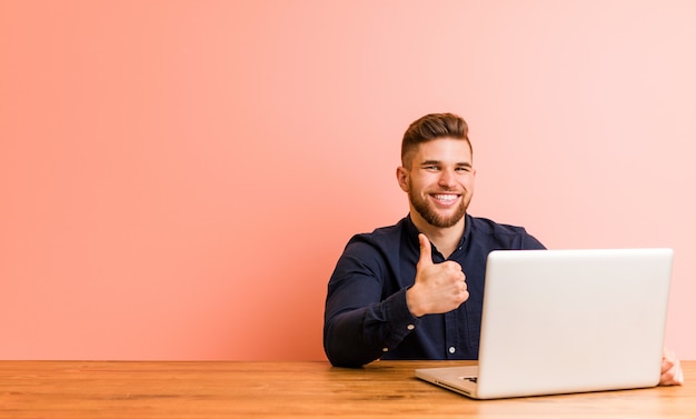 Jeune homme travaillant avec son ordinateur portable en souriant et en levant le pouce vers le haut