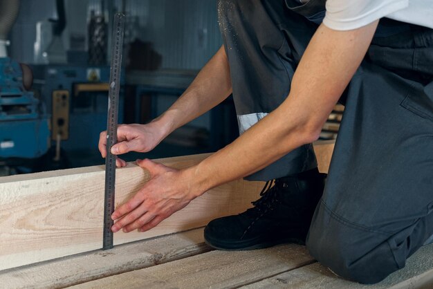 Un jeune homme travaille dans un atelier de menuiserie Un employé mesure du bois avec une règle