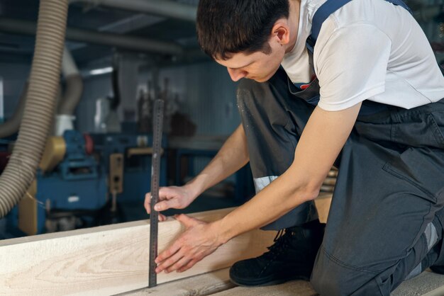 Un jeune homme travaille dans un atelier de menuiserie Un employé mesure du bois avec une règle