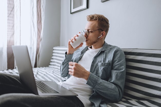 Un jeune homme travaille à la maison avec un ordinateur portable et boit du café