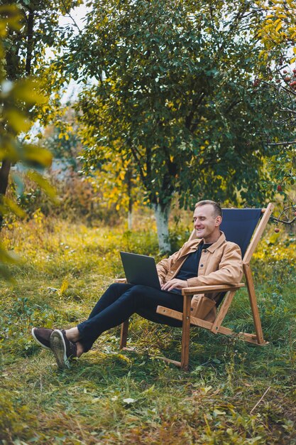 Photo un jeune homme travaille sur un ordinateur portable à l'extérieur un jeune pigiste se repose dans la forêt travail à distance loisirs actifs en été tourisme concept de personnes homme assis sur une chaise à l'extérieur