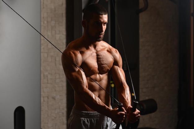 Jeune homme travaille sur sa poitrine avec câble croisé dans une salle de fitness moderne