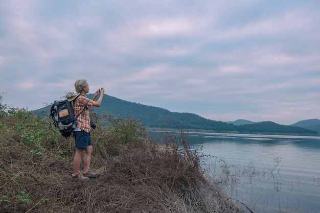 Jeune homme trekker utiliser smartphone prendre photo profiter de voyager avec sac à dos