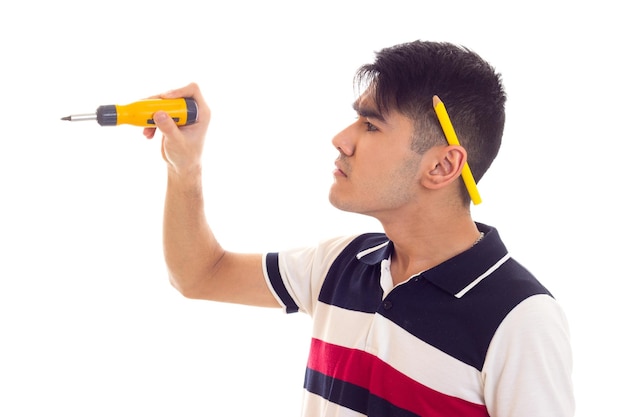 Jeune homme triste aux cheveux noirs avec un crayon derrière l'oreille tenant un tournevis jaune