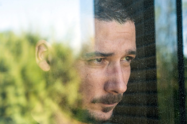 Photo jeune homme triste avec moustache derrière la vitre en dépression