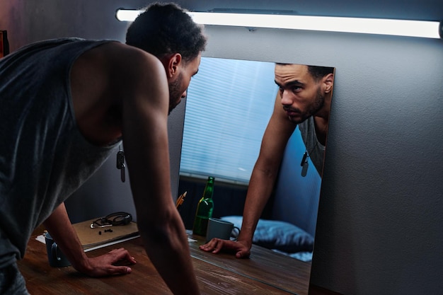 Jeune homme avec un trouble post-traumatique se penchant sur la table et regardant dans le miroir