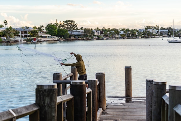 Jeune homme trowing un filet de pêche à l'eau d'un quai.