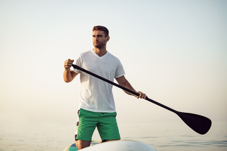 Photo jeune homme en tshirt et short flottant sur sup board