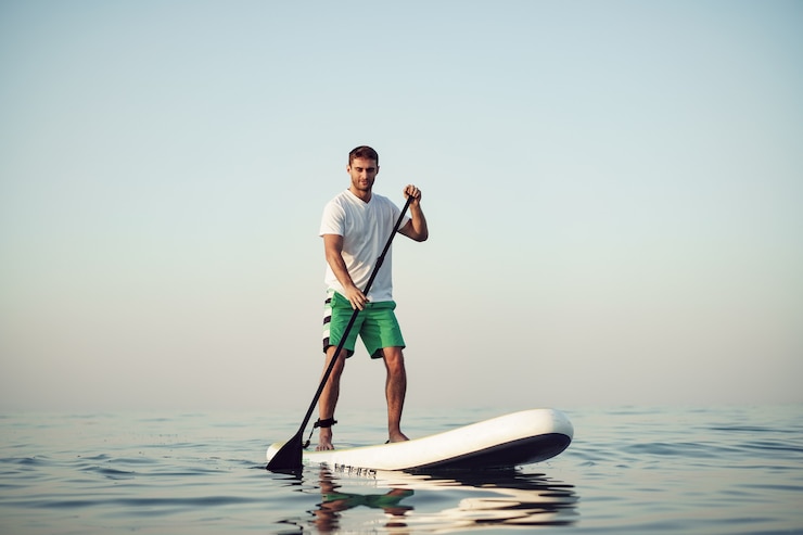 Photo jeune homme en tshirt et short flottant sur sup board