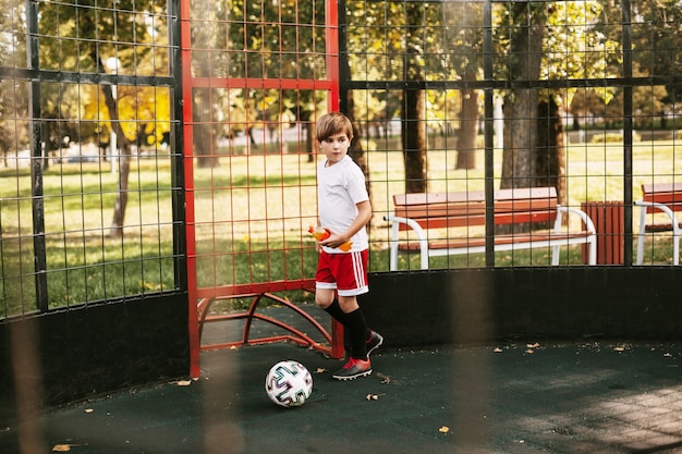 Photo un jeune homme en uniforme de sport s'entraîne avec un ballon sur le terrain de football freestyle.