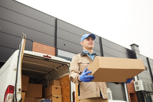 Jeune homme en uniforme transportant une grande boîte en carton il travaille dans la livraison de fret