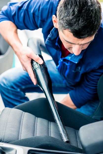 Jeune homme utilisant un aspirateur pour nettoyer l&#39;intérieur d&#39;une voiture