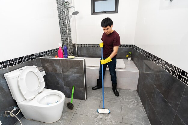 Jeune Homme Utilisant Une Brosse Pour Nettoyer Le Carrelage Dans La Salle  De Bain