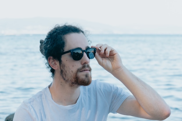 Jeune homme utilisant des lunettes de soleil souriant beaucoup en les touchant, concept de lunettes de soleil, été et voyage, espace de copie