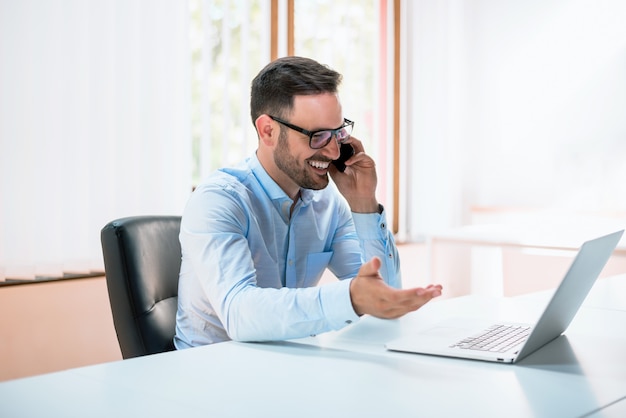 Jeune homme utilisant un ordinateur portable et parlant au téléphone