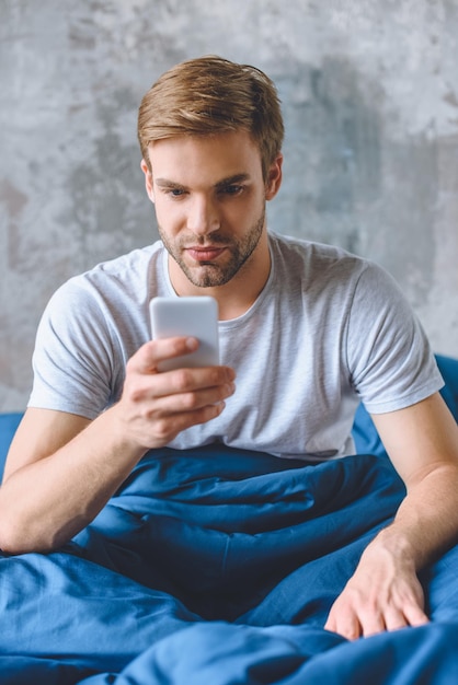 jeune homme utilisant un smartphone au lit à la maison