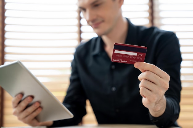 Jeune homme utilisant une tablette avec carte de crédit pour la banque en ligne, les achats en ligne, le commerce électronique par passerelle de paiement en ligne au bureau à domicile, les achats en ligne modernes et pratiques avec carte de débit, le dévoilement