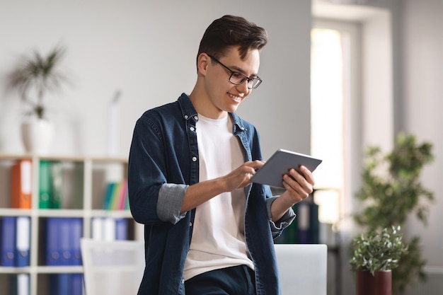 Jeune homme utilisant une tablette numérique debout près du bureau dans un bureau moderne