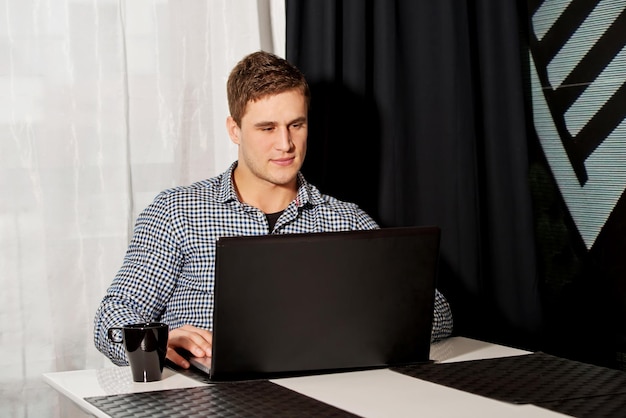 Un jeune homme utilise un ordinateur portable à la table du bureau.