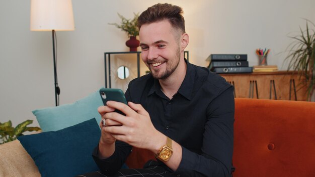 Un jeune homme utilise son téléphone alors qu'il est assis à la maison.