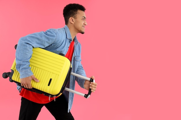 Jeune homme avec valise sur fond rose