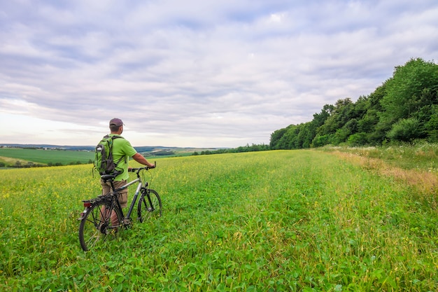 Jeune homme avec un vélo sur champ vert par une journée d'été ensoleillée