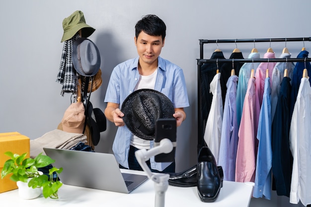 Jeune homme vendant un chapeau et des vêtements en ligne par smartphone en direct. Commerce électronique en ligne à domicile