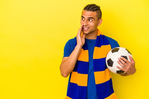 Un jeune homme vénézuélien regardant le football isolé sur fond jaune dit une nouvelle secrète de freinage à chaud et regarde de côté
