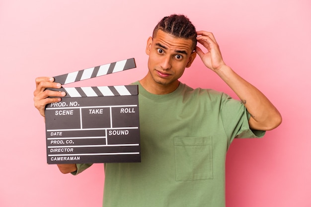 Jeune homme vénézuélien tenant un clap isolé sur fond rose étant choqué, elle s'est souvenue d'une réunion importante.