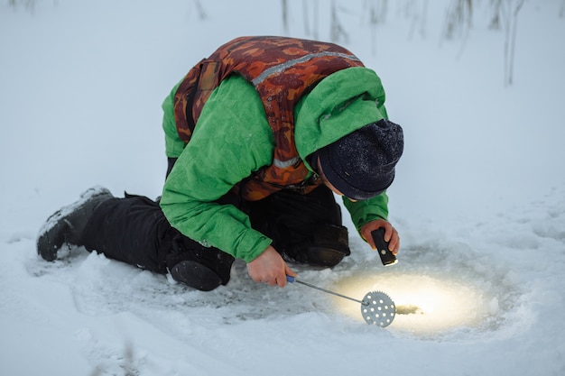 Jeune homme vérifie un trou dans un lac gelé sur un pêcheur d'hiver