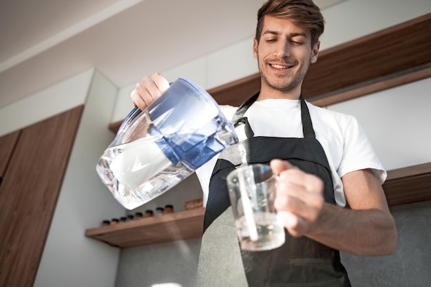 Le jeune homme verse de l'eau propre dans un verre