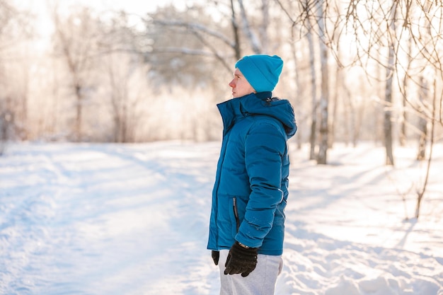 Un jeune homme en veste bleue se tient sur un chemin dans une forêt d'hiver enneigée