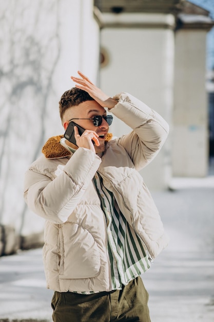 Jeune homme en veste d'hiver à l'aide de téléphone à l'extérieur de la rue