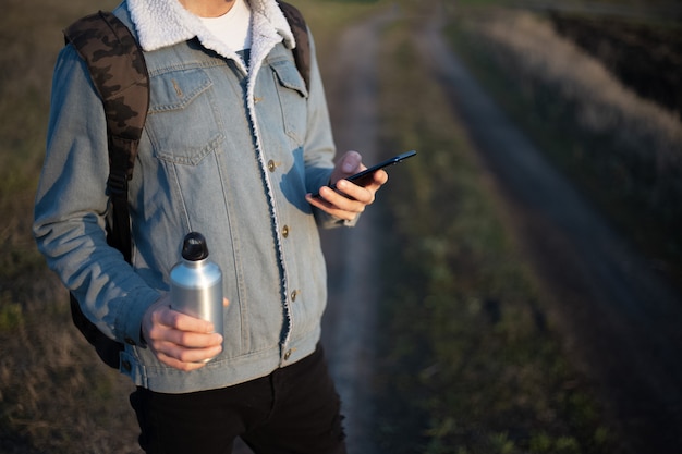 Jeune homme en veste en jean avec smartphone et bouteille en aluminium dans ses mains