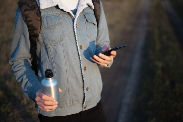 Jeune homme en veste en jean avec smartphone et bouteille en aluminium dans ses mains