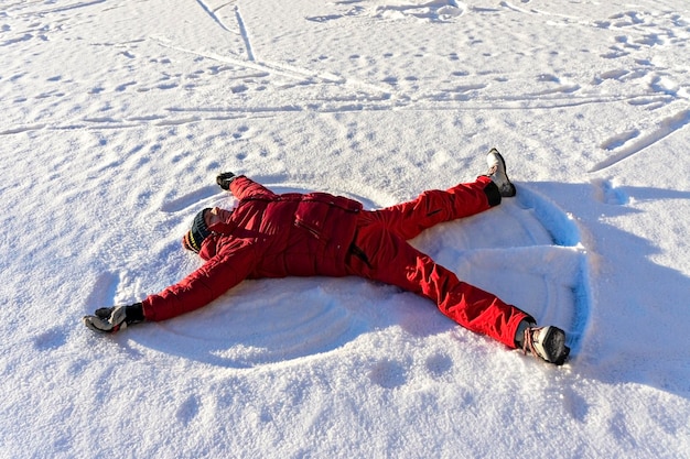 Jeune homme en vêtements chauds rouges allongé dans la neige et faisant un ange des neiges