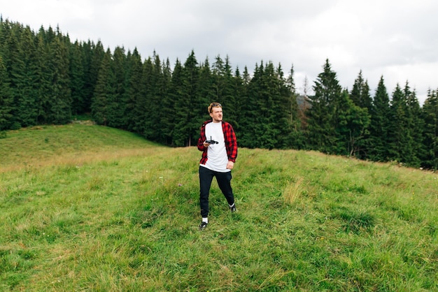 Jeune homme en vêtements décontractés se tient dans les montagnes sur un pâturage sur fond de forêt de montagne