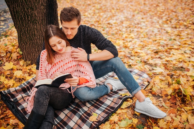 Jeune homme en vêtements noirs est assis sur une couverture et regarde la femme livre tient dans les mains