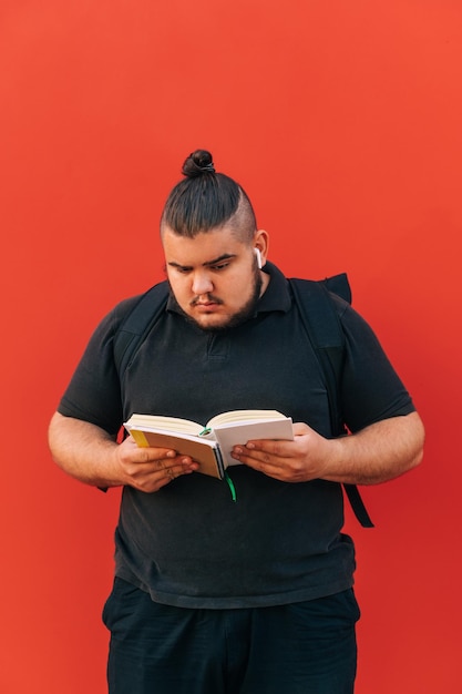 Jeune homme en vêtements noirs et en surpoids lit un livre sur fond rouge Vertical