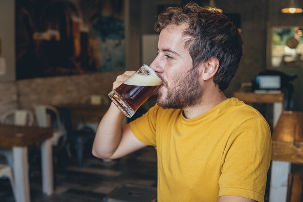 Jeune homme vêtu d'une chemise jaune vif, boire de la bière seul dans un pub