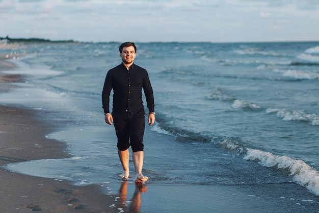Un jeune homme vêtu d'une chemise noire marche le long de la mer le soir