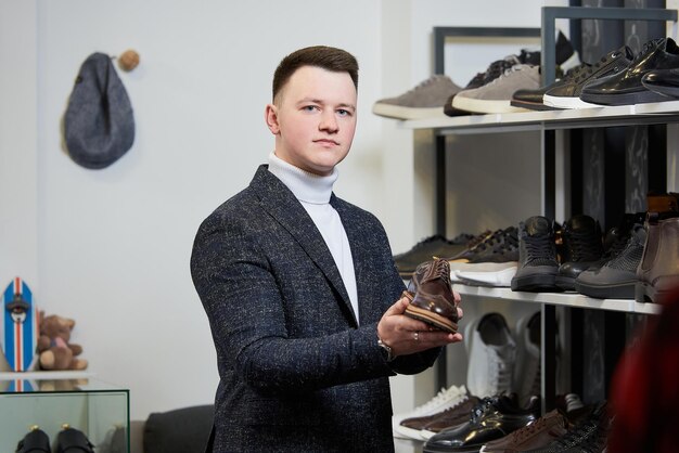 Photo un jeune homme vêtu d'un pull à col roulé blanc et d'un costume choisit des chaussures dans un magasin de vêtements un client masculin dans une boutique