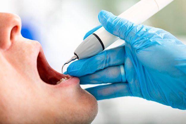 Jeune homme visitant le cabinet dentaire Dentiste mains dans des gants de protection examinant les dents du patient